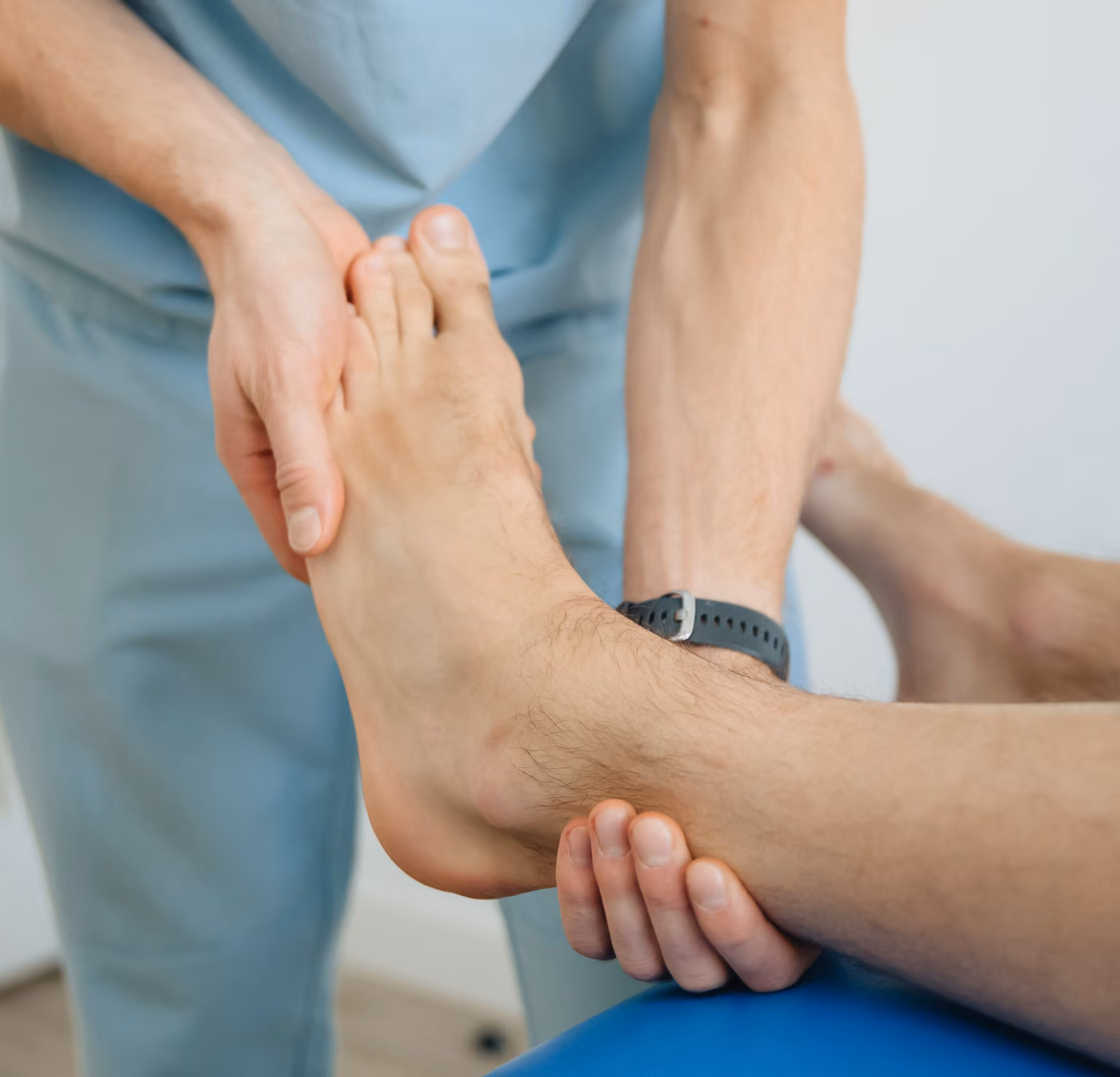 A healthcare professional examines a patient's ankle with both hands.
